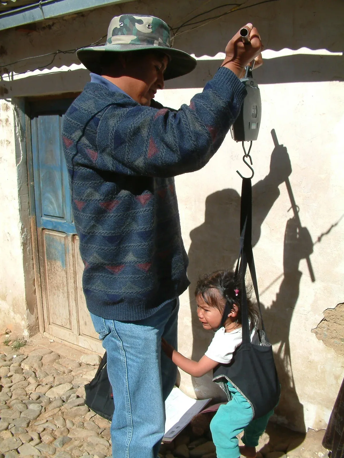 A community health worker in El Alto, Bolivia, weighing a child with a hanging scale for growth monitoring
