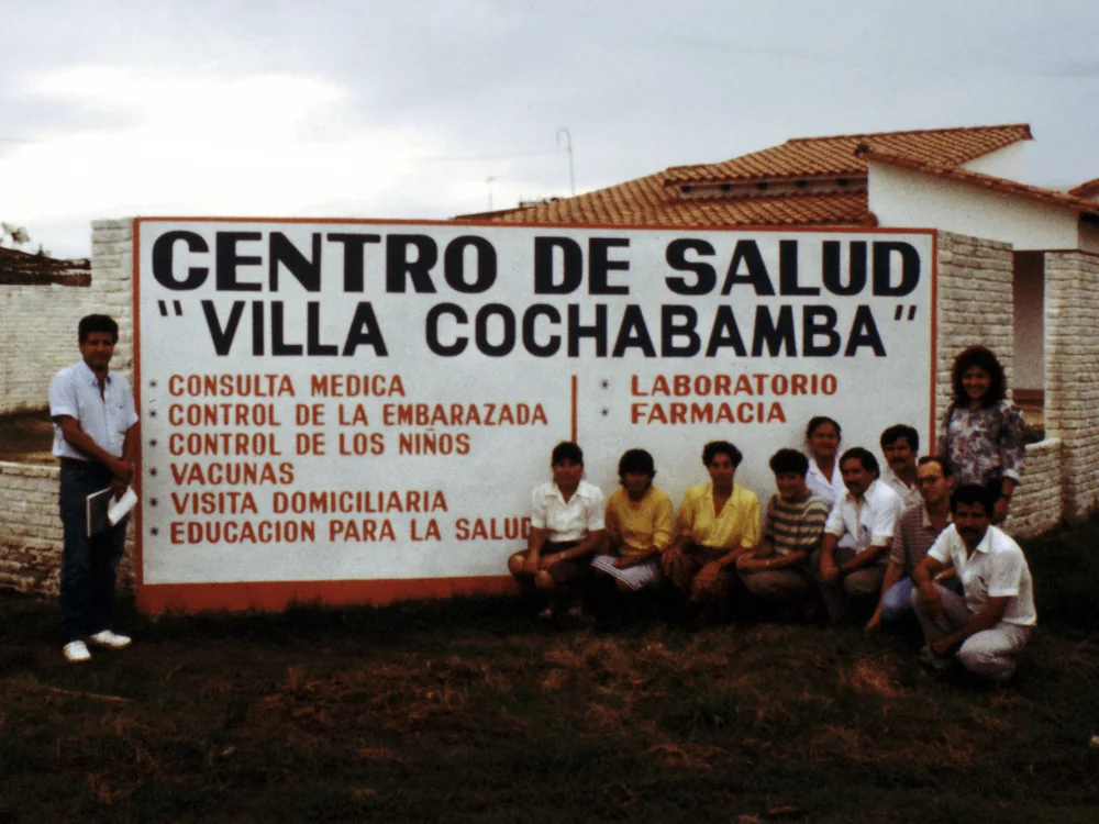 Health center staff gathered beside the Centro de Salud "Villa Cochabamba" sign listing its services, Bolivia