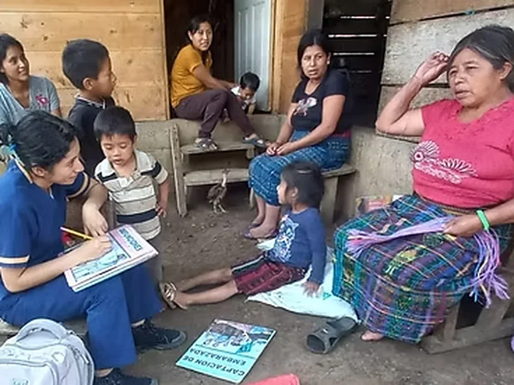 A health worker counsels a mother using a flipchart while families gather outside a home in rural Guatemala